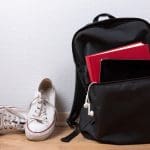 Old white sneakers, book and tablet with earphones in backpack on wooden background